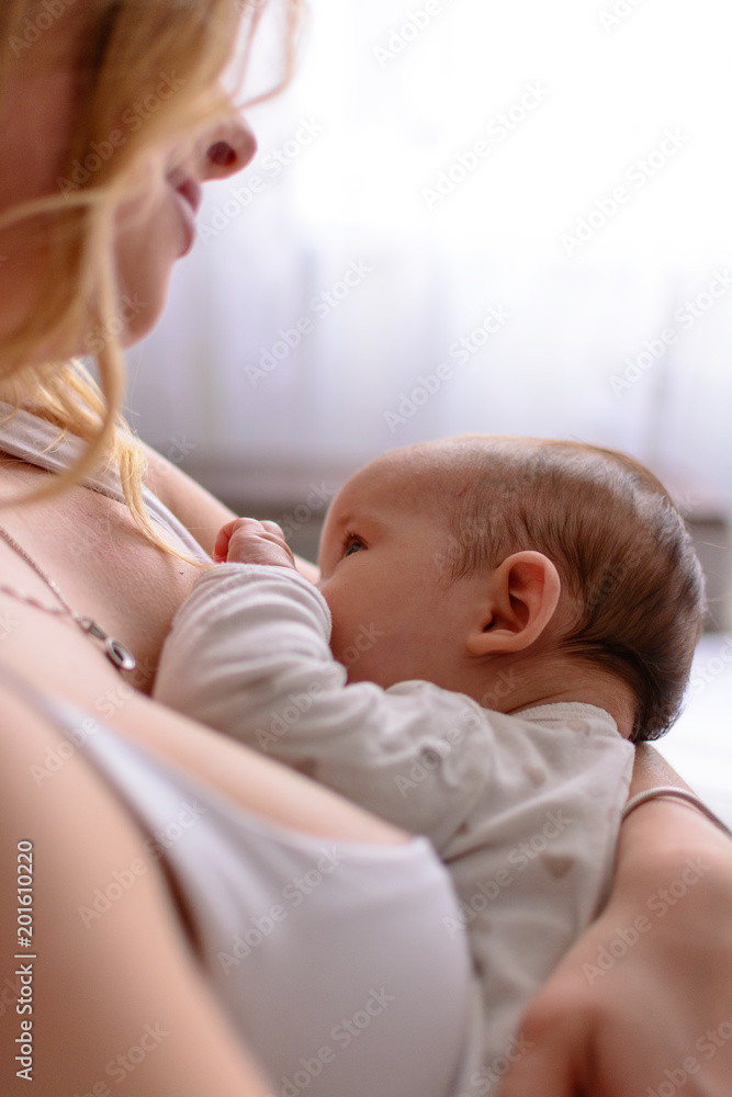 Breastfeeding baby close up. Pretty mother holding her newborn child. Mom nursing baby. Beautiful woman and new born relax at home. Blondе mother breast feeding baby.