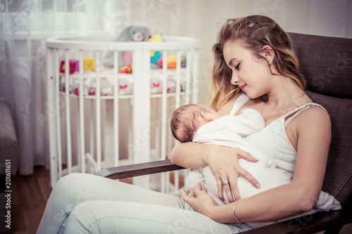 Obraz na płótnie Breastfeeding baby near crib. Pretty mother holding her newborn child. Mom nursing baby. Beautiful woman and new born relax at home in nursery interior. Blondе mother breast feeding baby. w salonie
