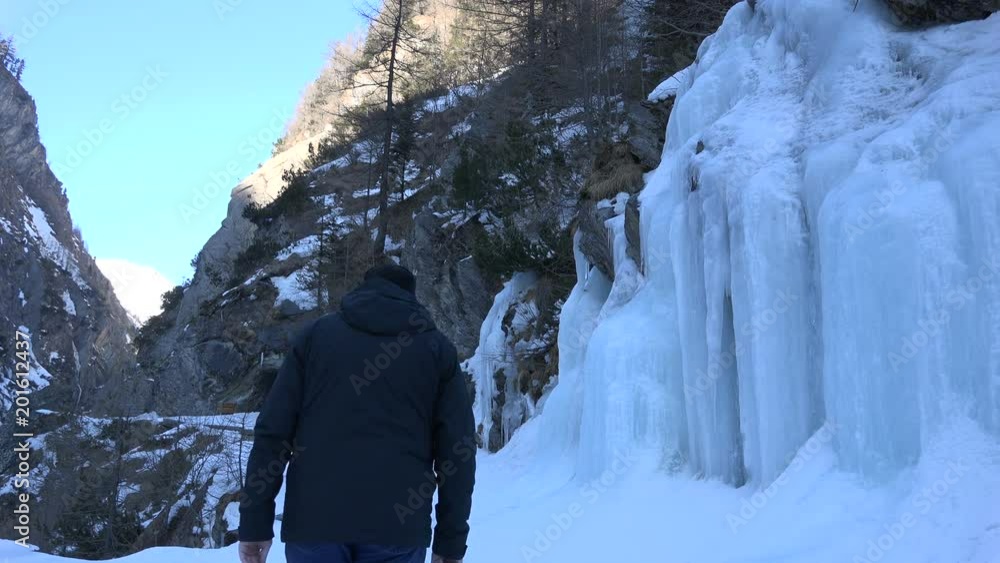 Senior man passing one of the many frozen waterfall cascades in the Dabaklamm, a very steep and narrow gorge in the Hohe Tauern nature reserve mountain region, Tirol Austria in winter. Senior man passing one of the many frozen waterfall cascades in the Dabaklamm, a very steep and narrow gorge in the Hohe Tauern nature reserve mountain region, Tirol Austria in winter.