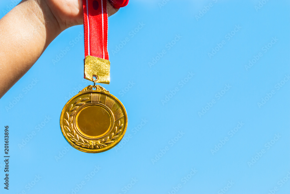 Winners success award concept : Champion hand holding gold medals reward against blue sky background. Winning at sport games show success. Winners success award concept : Champion hand holding gold medals reward against blue sky background. Winning at sport games show success.