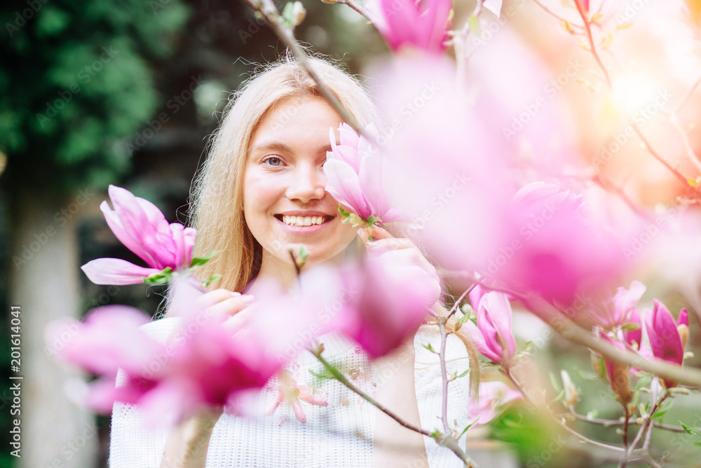 Fototapeta premium Close up portrait of happy blond smiling woman with blooming magnolia. Happy moment concept.