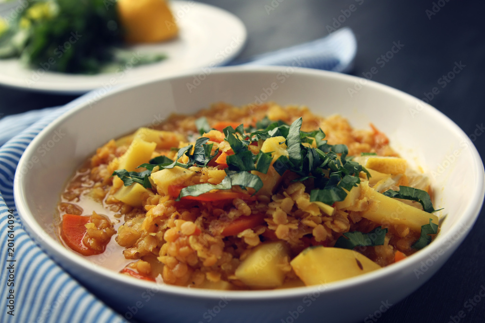 Red lentil stew with potato, carrot and turmeric. Toned photo. Healthy lunch on the round white plate. Colorful vegan dish with potato, carrot and turmeric. European cuisine. Vegetarian.