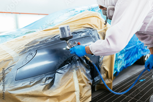 Foto Man with protective clothes and mask painting car using spray compressor