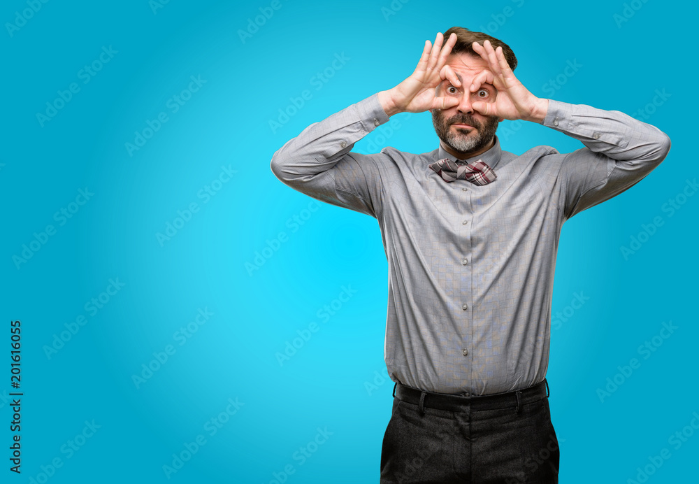 Middle age man, with beard and bow tie looking at camera through fingers in ok gesture. Imitating binoculars Middle age man, with beard and bow tie looking at camera through fingers in ok gesture. Imitating binoculars