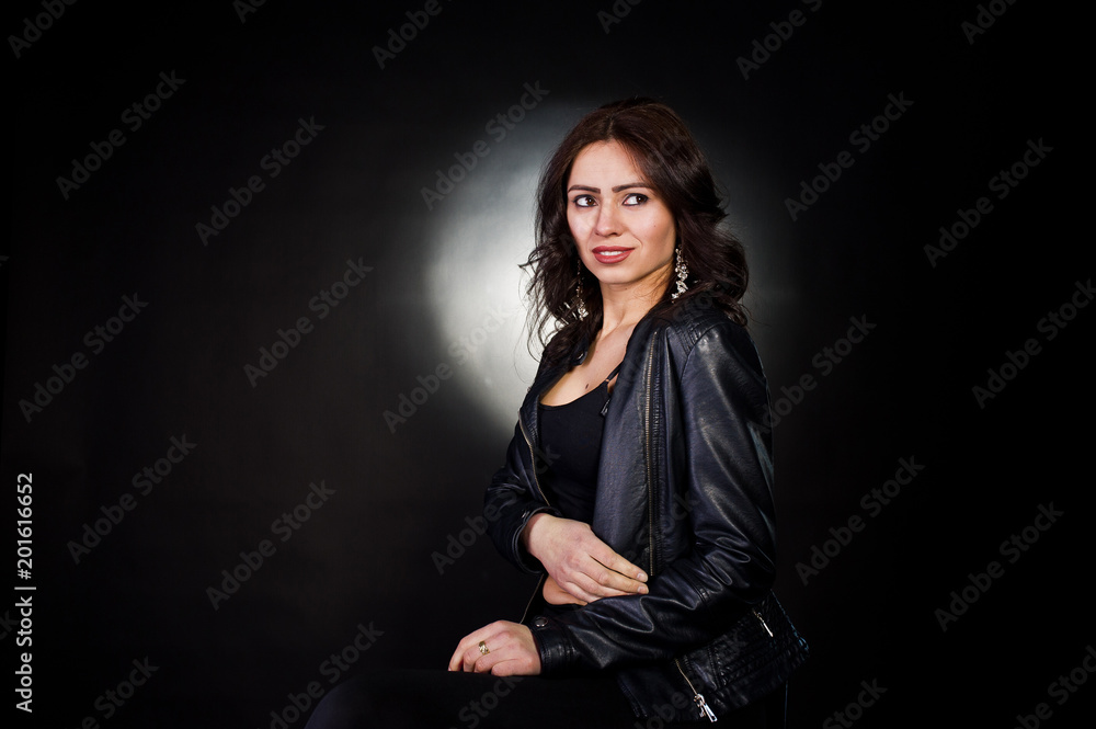 Studio portrait of sexy brunette girl in black leather jacket against black background.