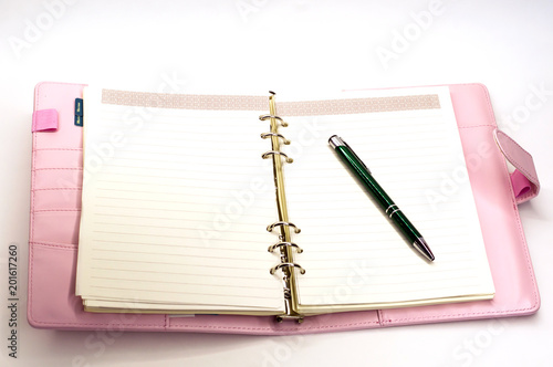 pink notebook with a ballpoint pen lying on white background