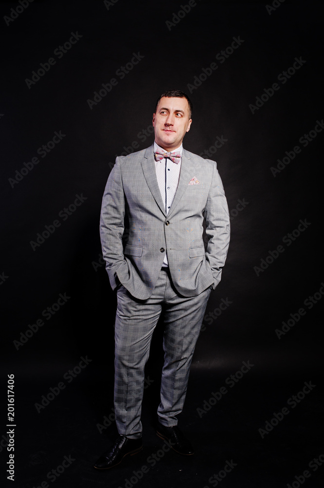 Fototapeta premium Studio portrait of man in gray suit and bow tie against black background.