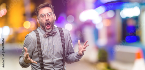 Middle age man, with beard and bow tie happy and surprised cheering expressing wow gesture at night club