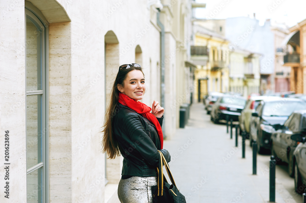 Fototapeta premium Portrait of a young beautiful woman, girl posing on the streets of a European city . The model is dressed in a stylish leather jacket