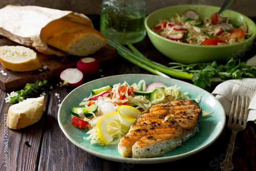 Grilled salmon steak and vegetarian vegetable salad of radish, cucumbers, lettuce salad. on a wooden table. Healthy proper nutrition.