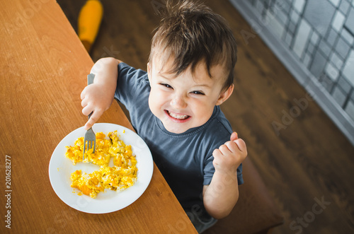 a child in a t-shirt in the kitchen eating an omelet, a fork