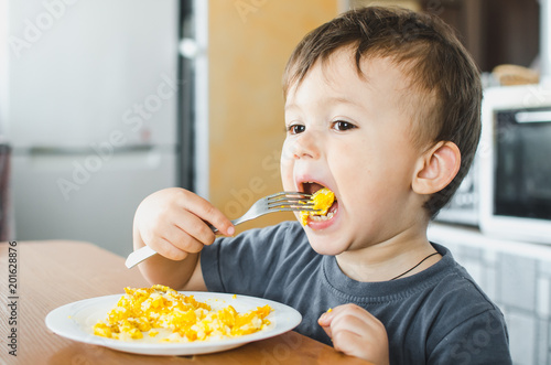 a child in a t-shirt in the kitchen eating an omelet, a fork