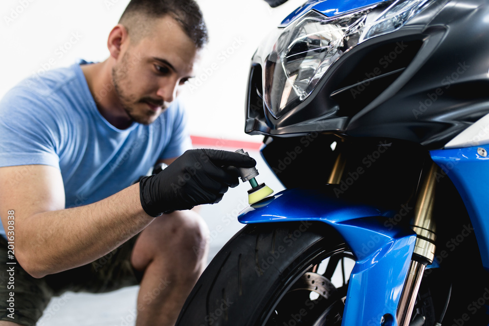 Naklejka premium Motorcycle detailing - Man with orbital polisher in repair shop polishing motorcycle. Selective focus.