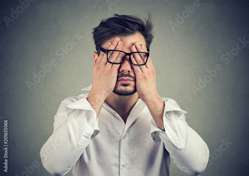 young man in glasses covering face eyes with both hands