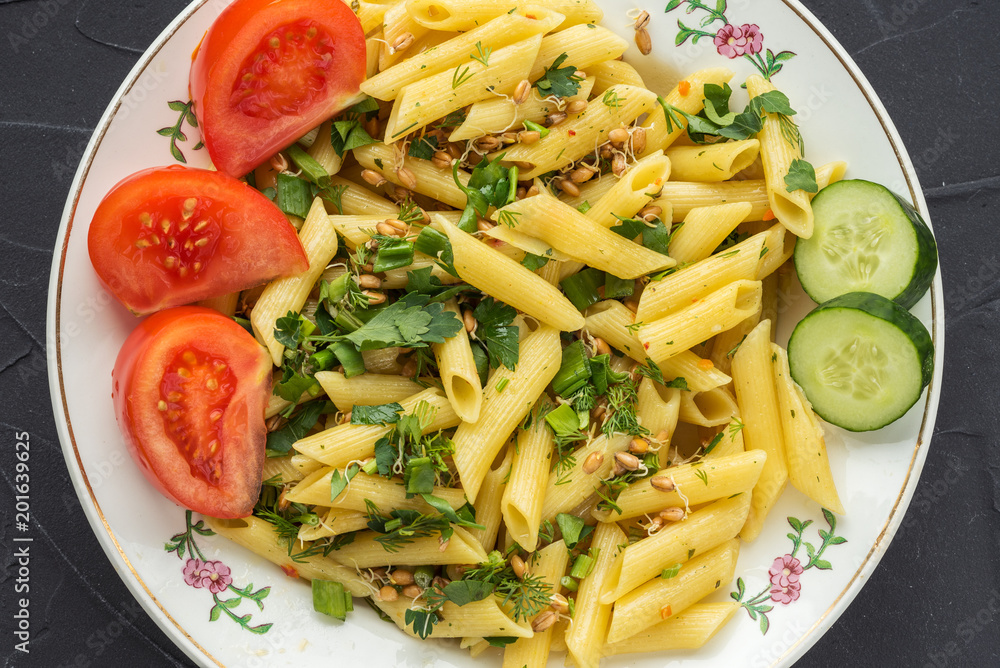 Plate with pasta, seasoned with dill parsley and greens, sliced cucumbers. View from the top, a black background.