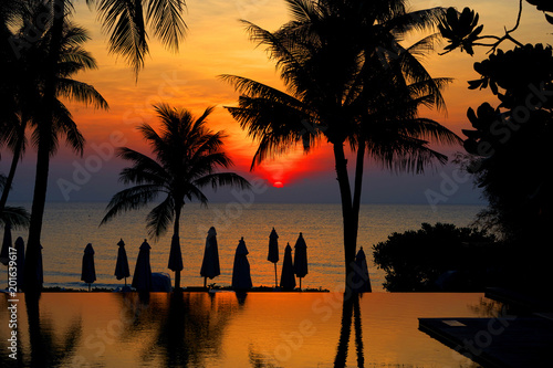 Sun rise at beach front with silhouette coconut or palm tree ,umbrella and pool with reflection
