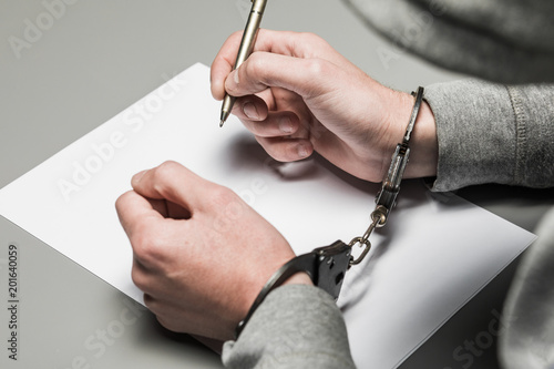 Hands of the criminal in handcuffs write a handle on paper. Sincere confession, request, statement. Justice