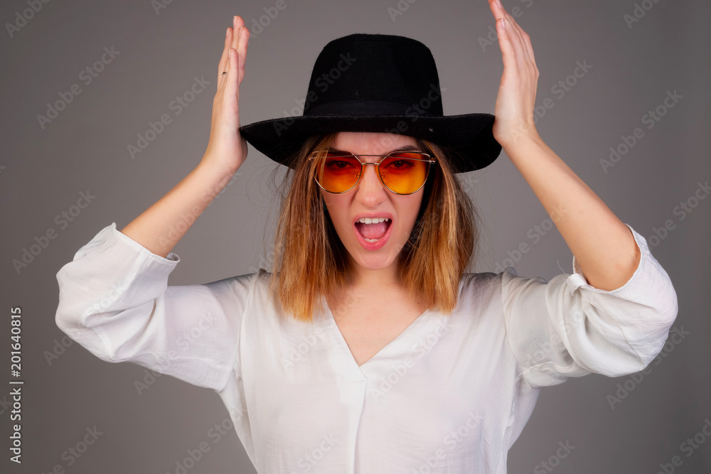 Portrait of fashionable girl with a hat on her head on gray background. The girl grimaces looks at the camera Portrait of fashionable girl with a hat on her head on gray background. The girl grimaces looks at the camera