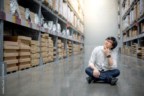 Young Asian man sitting in warehouse choosing what to buy, shopping warehousing concept