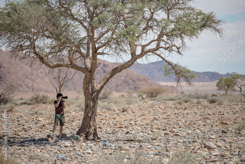 Young male traveler and photographer taking photo of African animals under the Savanna tree in Namibia. Wildlife photography concept.