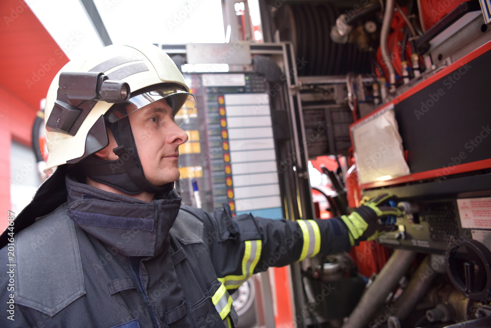 Fototapeta premium Feuerwehrmann bedient Technik am Löschfahrzeug zur Bekämpfung von Hausbränden // Firefighter operates technology on fire engine to fight house fires