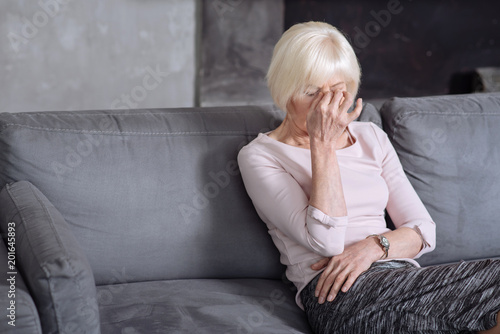 Fotografía Mature sorrowful woman sitting on the sofa and having headache.