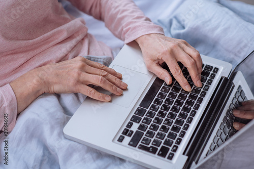 Mature busy woman sitting on the bed and using laptop.