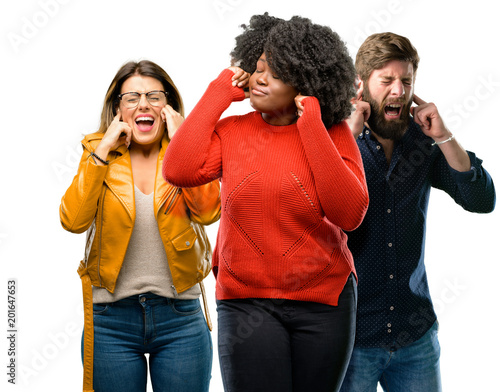 Group of three young men and women covering ears ignoring annoying loud noise, plugs ears to avoid hearing sound. Noisy music is a problem.
