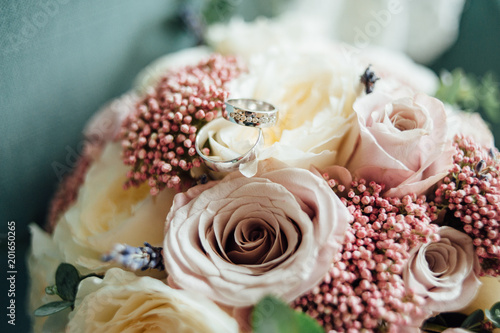 Wedding rings of white metal with diamonds on a wedding bouquet of flowers with white and pink roses