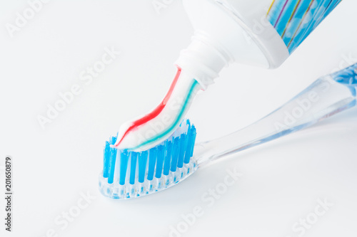 toothbrush of clear plastic with blue bristles, white blue red toothpaste squeezes out of a tube