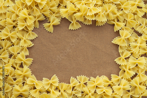 farfalle macaroni background of pasta. A textured wooden cutting board. Close-up view from the top. Free space for text. White frame for text.