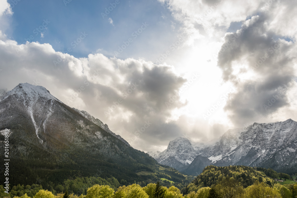 Fototapeta premium Die Sonne scheint durch die Wolken auf Berge im Frühling