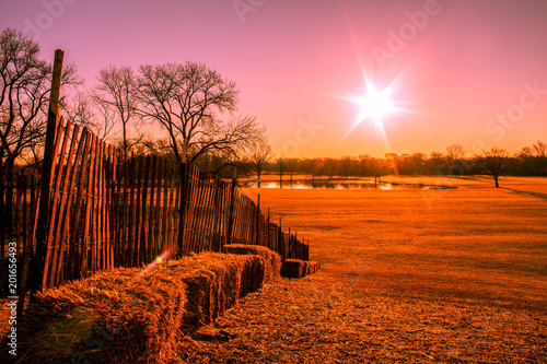 pink toned sunrise on the hill with a wood fence and straw bales