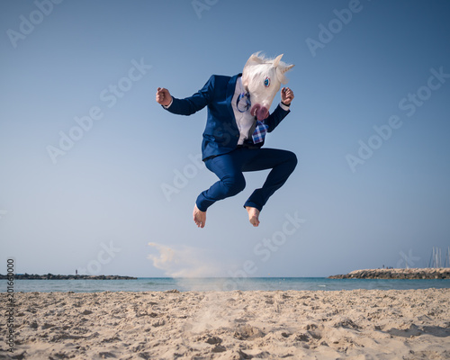 Stylish man in funny mask and suit jumps on beach