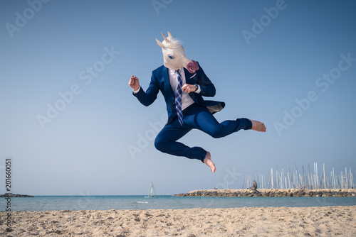 Stylish manager in funny mask and elegant suit jumps on beach