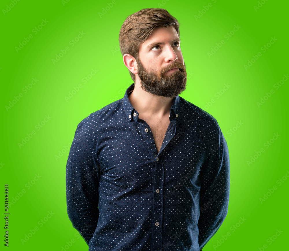 Obraz premium Young hipster man with big beard doubt expression, confuse and wonder concept, uncertain future over green background