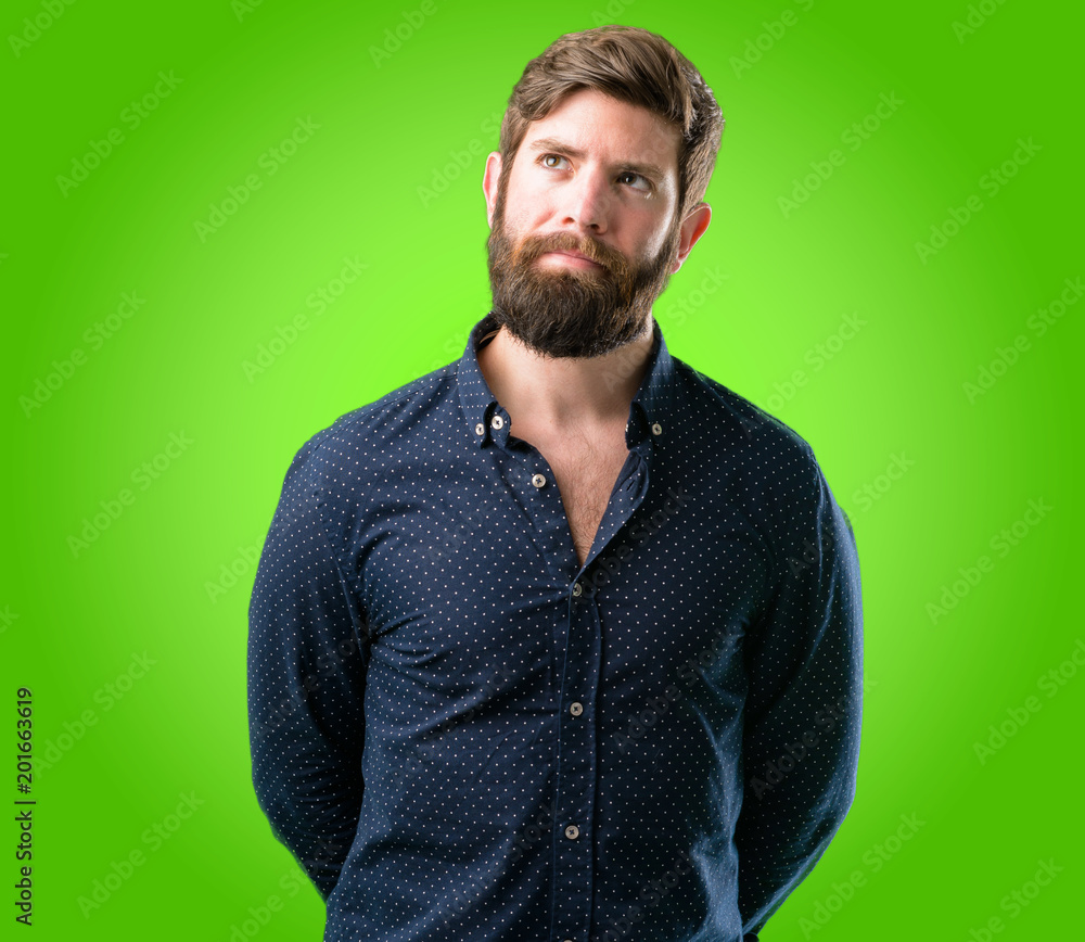 Fototapeta premium Young hipster man with big beard doubt expression, confuse and wonder concept, uncertain future over green background
