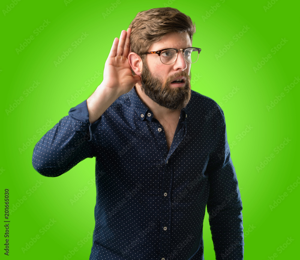 Young hipster man with big beard holding hand near ear trying to listen to interesting news expressing communication concept and gossip over green background Young hipster man with big beard holding hand near ear trying to listen to interesting news expressing communication concept and gossip over green background