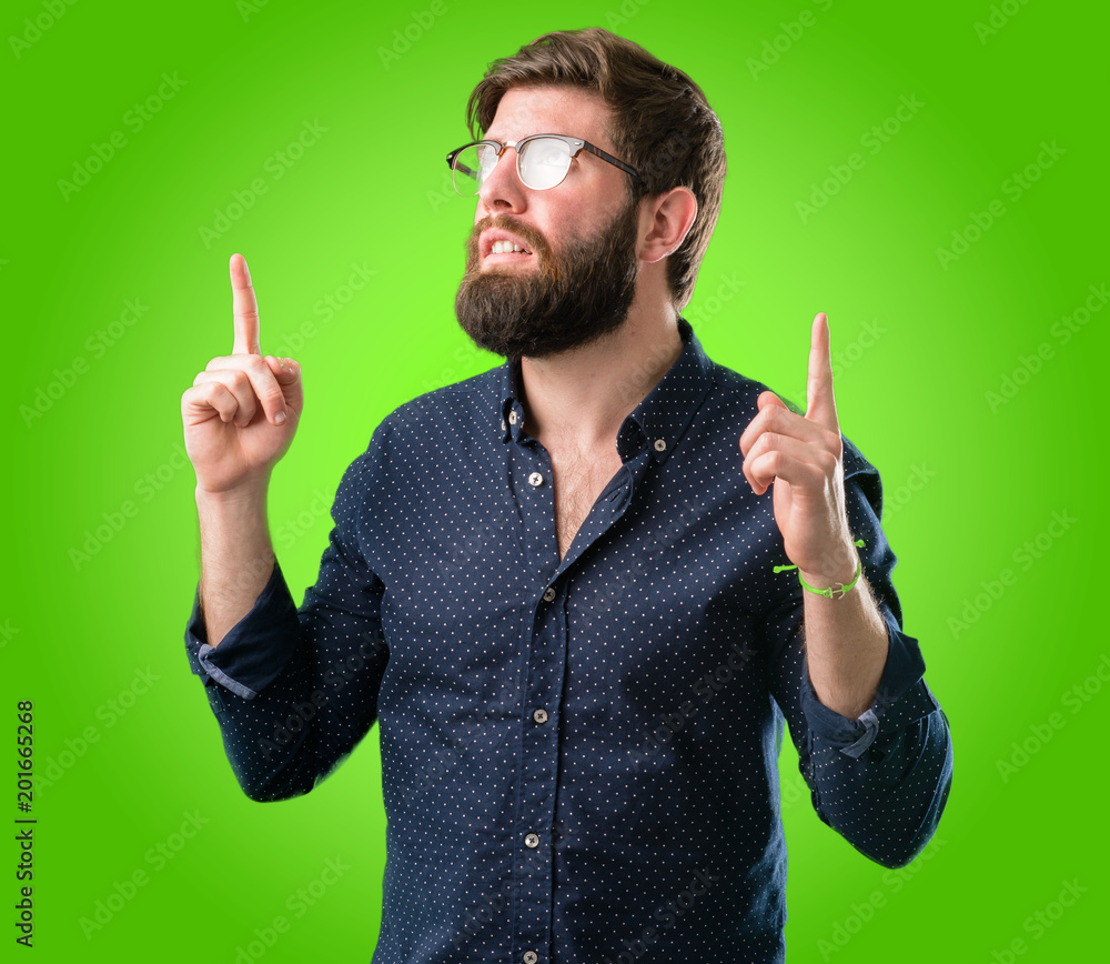 Young hipster man with big beard happy and surprised cheering pointing up over green background Young hipster man with big beard happy and surprised cheering pointing up over green background