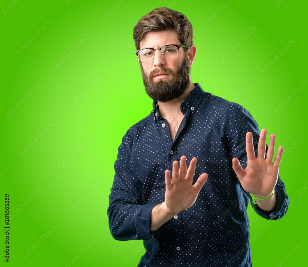 Young hipster man with big beard annoyed with bad attitude making stop sign with hand, saying no, expressing security, defense or restriction, maybe pushing over green background Young hipster man with big beard annoyed with bad attitude making stop sign with hand, saying no, expressing security, defense or restriction, maybe pushing over green background