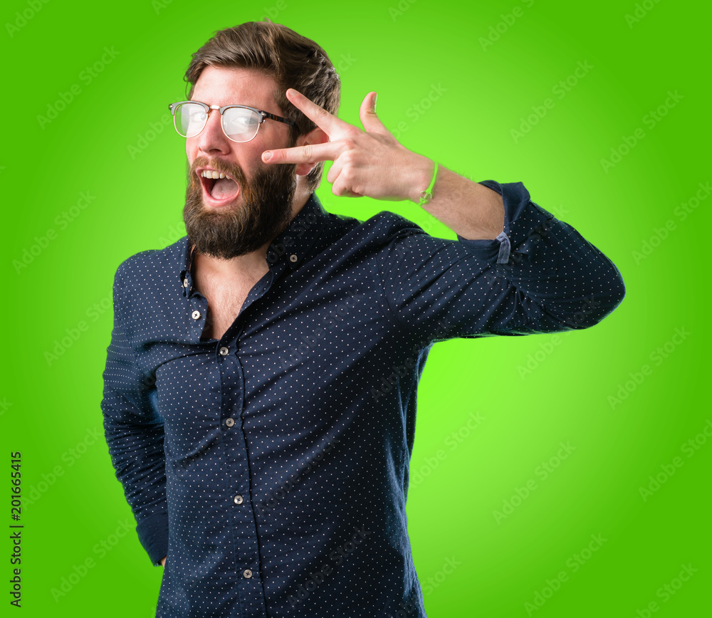 Young hipster man with big beard looking at camera through her fingers over green background Young hipster man with big beard looking at camera through her fingers over green background