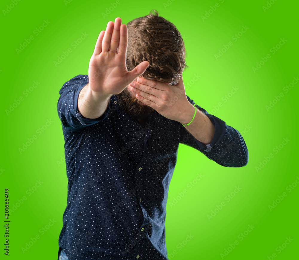 Young hipster man with big beard stressful and shy keeping hand on head, tired and frustrated over green background Young hipster man with big beard stressful and shy keeping hand on head, tired and frustrated over green background