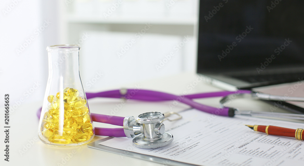 closeup of the desk of a doctors office with a stethoscope in the foreground and a bottle with pills in the background closeup of the desk of a doctors office with a stethoscope in the foreground and a bottle with pills in the background