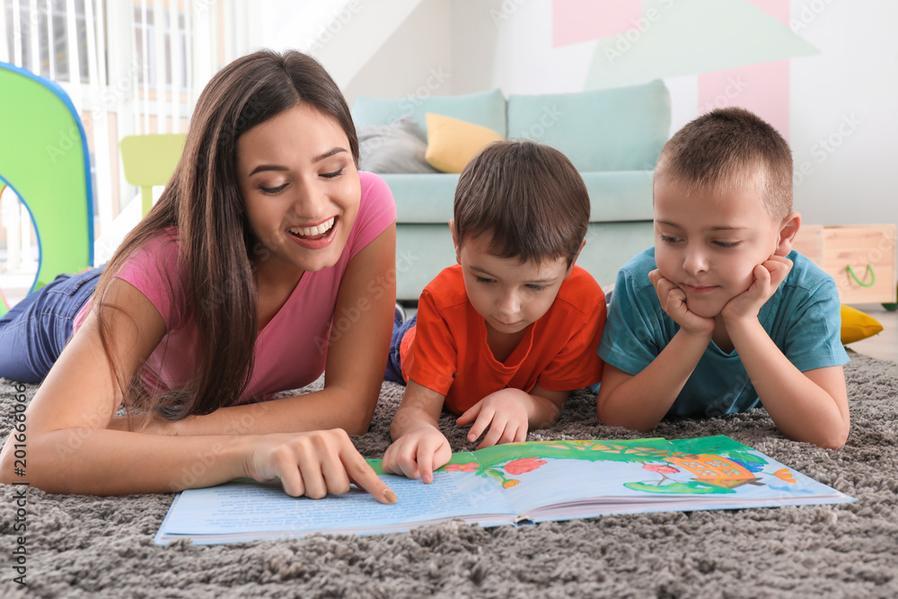 Fototapeta premium Two little boys reading book with nanny at home
