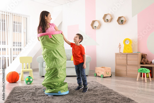 Nanny and little boy playing with toy tunnel at home photo