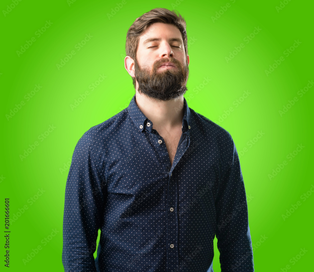 Obraz premium Young hipster man with big beard with sleepy expression, being overworked and tired over green background