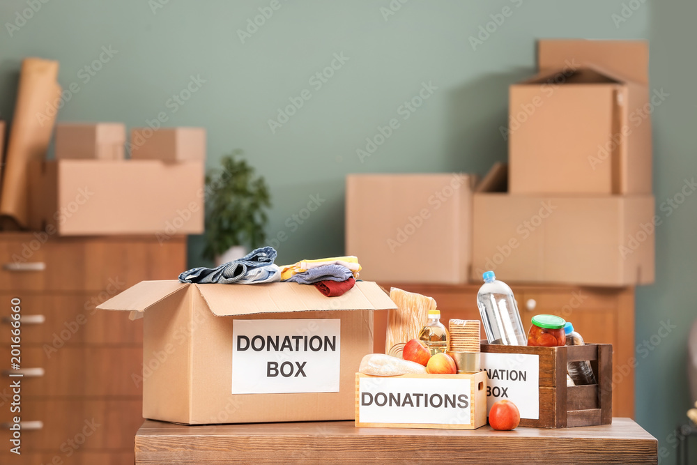 Donation boxes with food products and clothes on table indoors Donation boxes with food products and clothes on table indoors