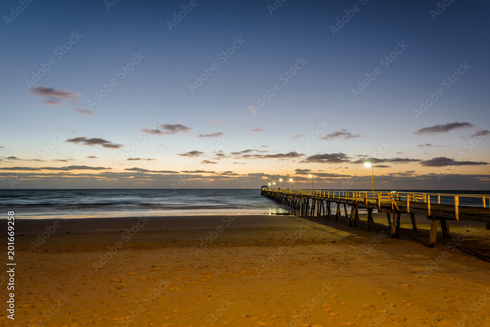 Beautiful colorful sunset summer view to the calm great ocean with pure sandy beach and a lovely empty wooden jetty lighten the night at a public boulevard, Glenelg Jetty, Adelaide, South/ Australia
