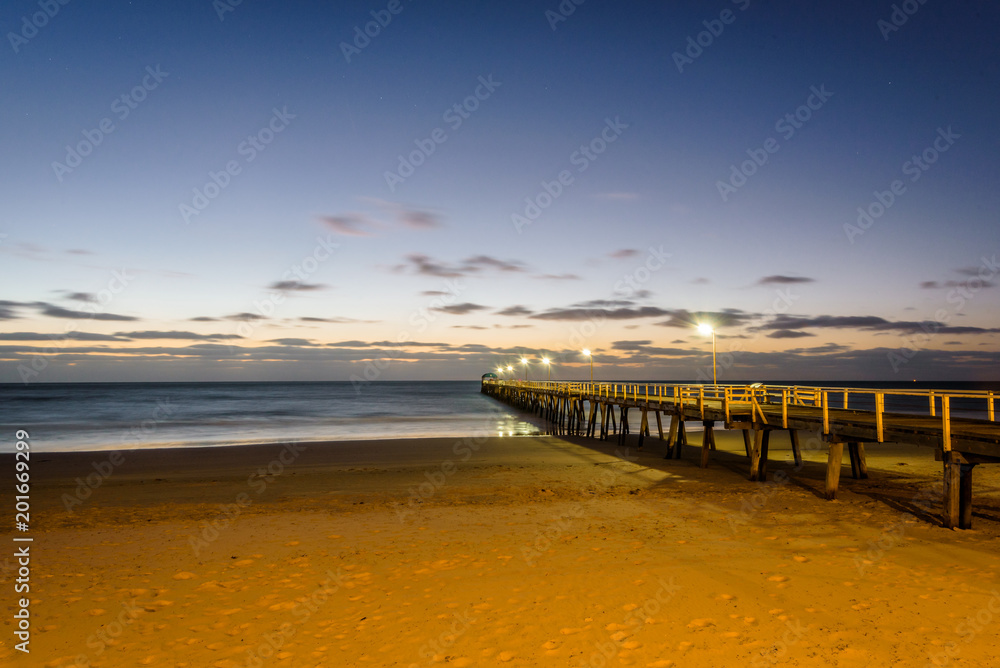 Beautiful colorful sunset summer view to the calm great ocean with pure sandy beach and a lovely empty wooden jetty lighten the night at a public boulevard, Glenelg Jetty, Adelaide, South/ Australia