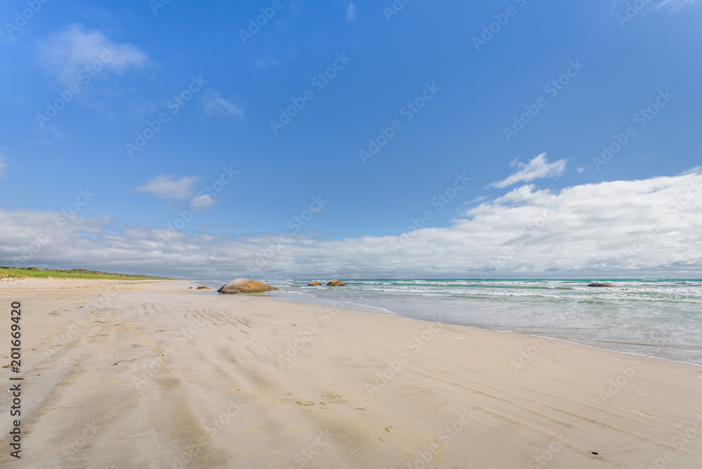 Beautiful sunny coast view to the australian blue sea with waves water and sandy beach at an empty place surrounded by rocks hills granite boulders at shore, Cape Jaffa, Great Ocean, South Australia,